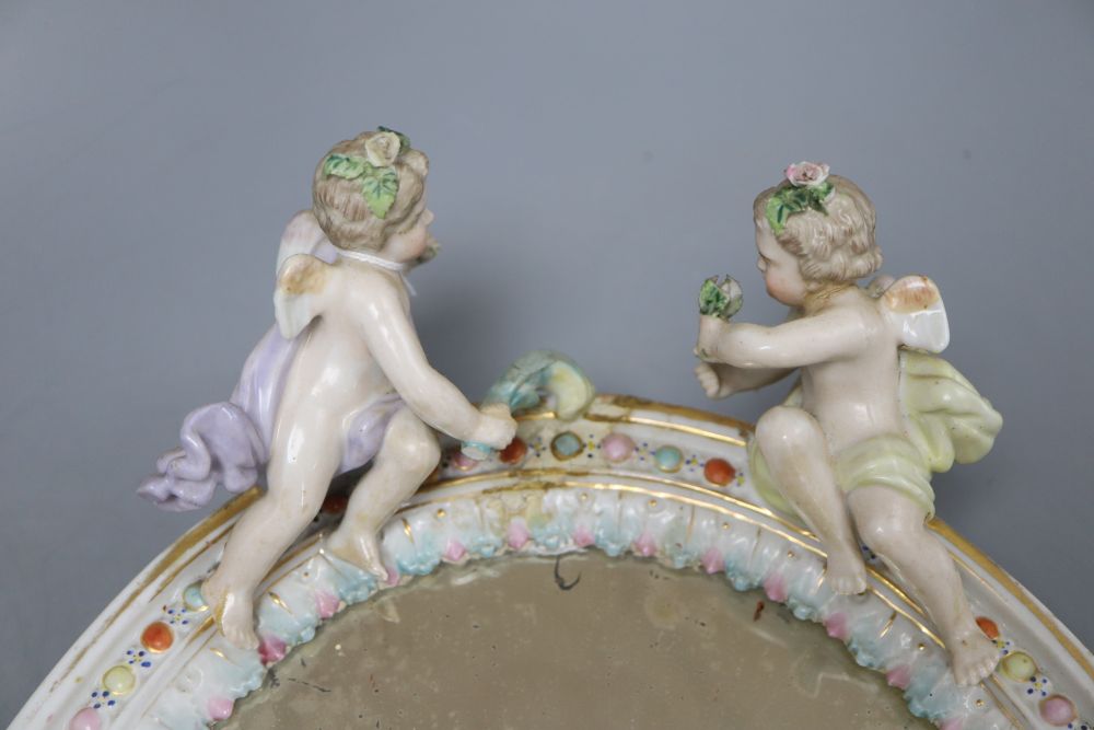 A German floral encrusted porcelain wall mirror, surmounted with winged cherubs, overall length 33cm